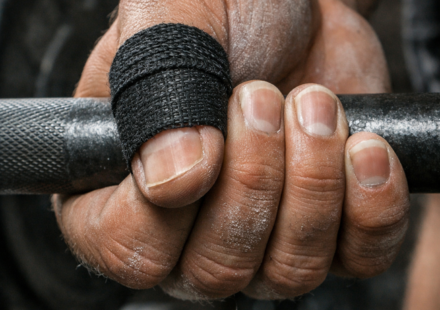 Mano con pulgar vendado sujetando una barra de pesas